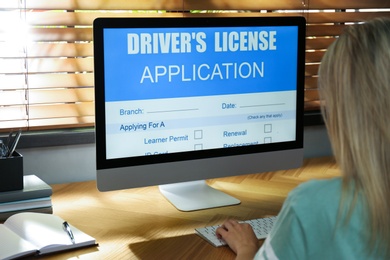 Photo of Woman using computer to fill driver's license application form at table in office, closeup
