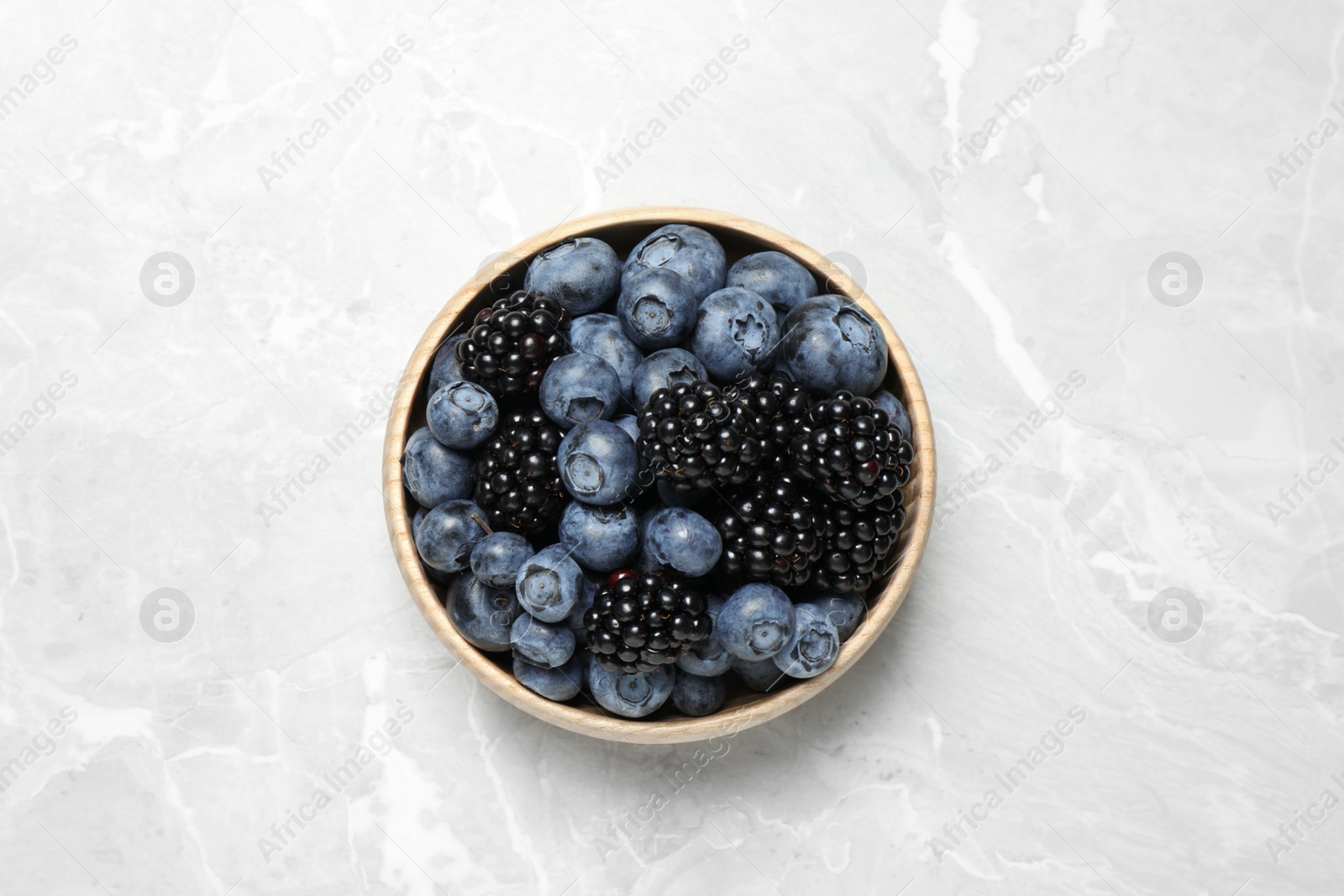 Photo of Blueberries and blackberries on light marble table, top view