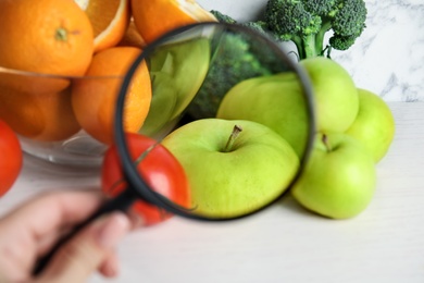 Photo of Woman with magnifying glass exploring vegetables and fruits, closeup. Poison detection