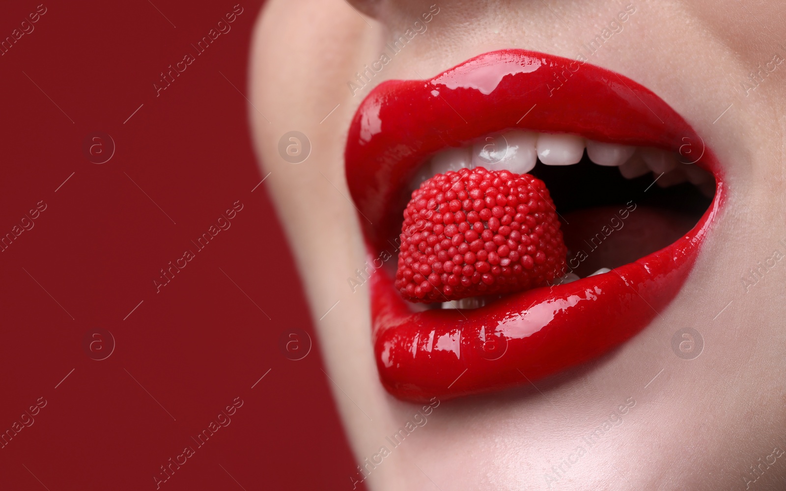 Photo of Closeup view of beautiful young woman with perfect lips makeup eating candy on red background