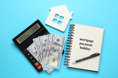 Photo of Notebook with words Mortgage Payment Holiday, house model, calculator and money on light blue background, flat lay