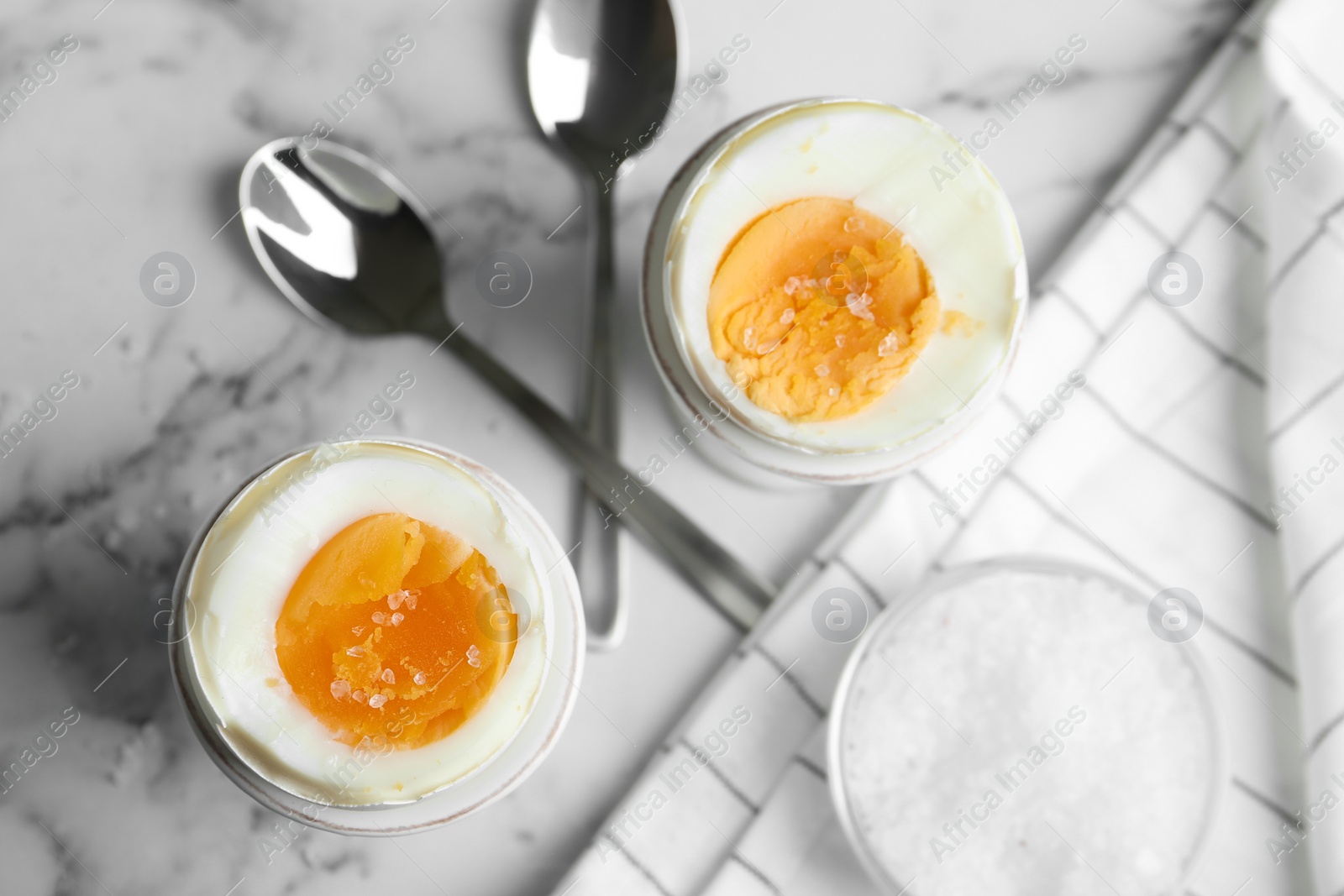 Photo of Tasty medium boiled eggs in ceramic holders on white marble table, flat lay