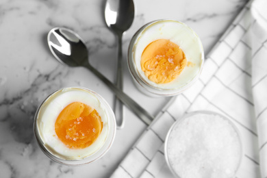 Photo of Tasty medium boiled eggs in ceramic holders on white marble table, flat lay