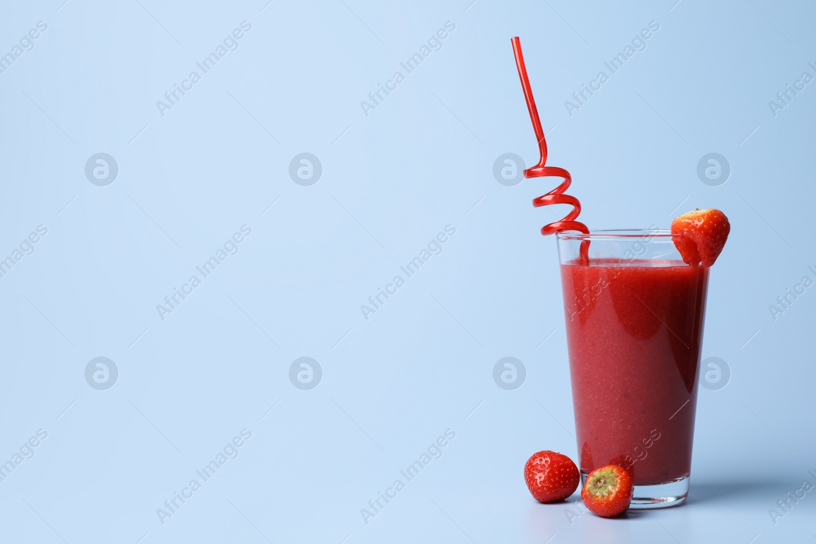 Photo of Glass with delicious berry smoothie and fresh strawberries on light blue background. Space for text