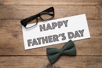 Photo of Card with phrase HAPPY FATHER'S DAY, eyeglasses and bow tie on wooden background, flat lay