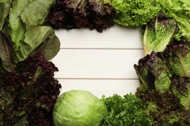 Photo of Frame made with different sorts of lettuce on white wooden table, top view. Space for text