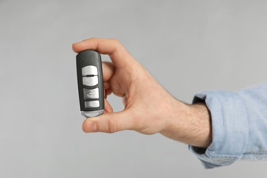 Young man holding car smart key on grey background, closeup