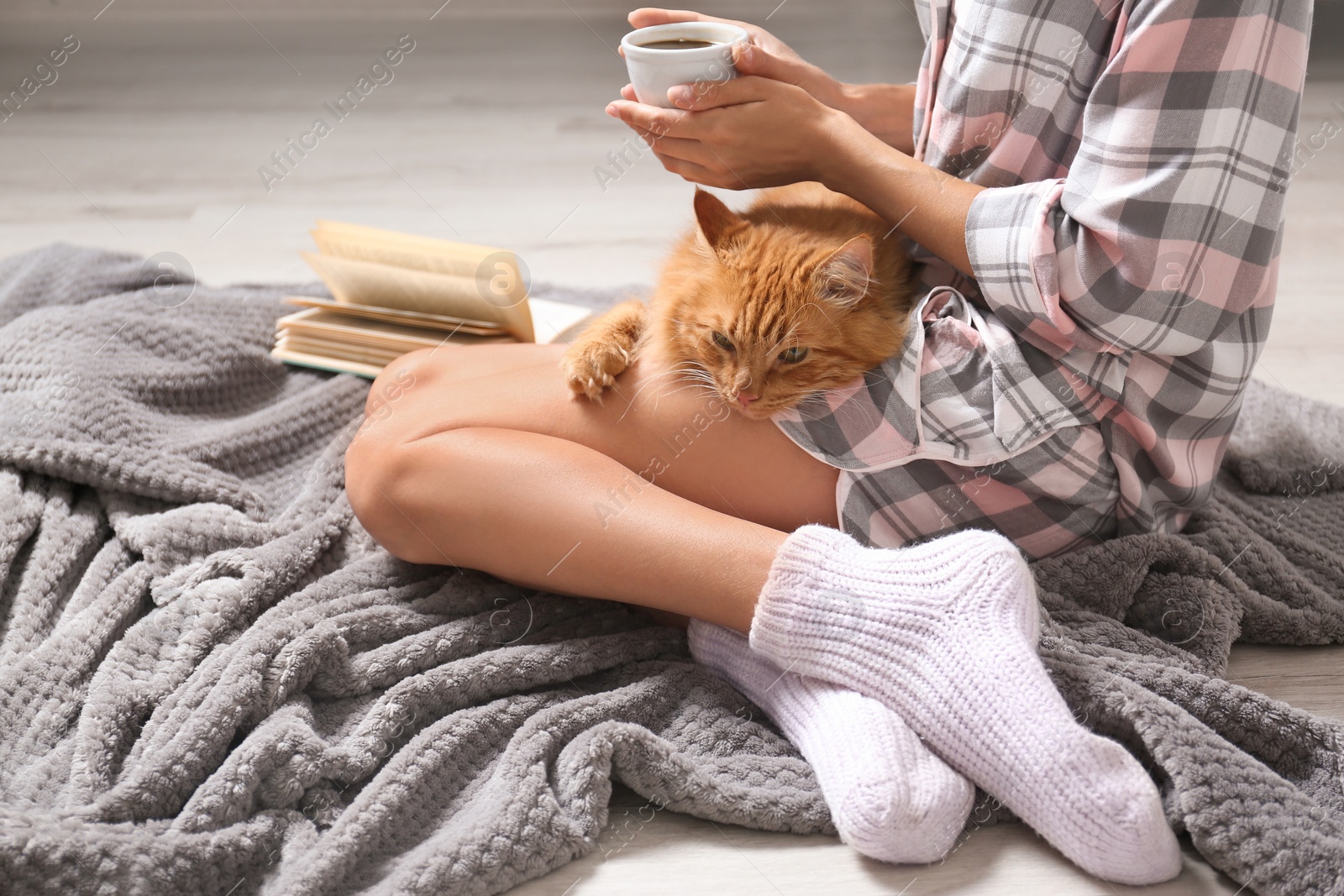 Photo of Woman with cute red cat and book on grey blanket at home, closeup view. Space for text