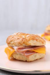 Photo of Delicious bagel with ham and cheese on light grey table, closeup