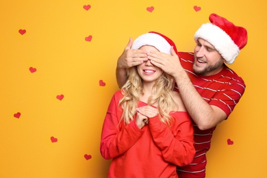Photo of Young couple in Santa hats on color background. Christmas celebration