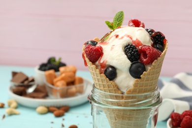 Photo of Delicious ice cream with berries in wafer cone served on light blue table, closeup. Space for text