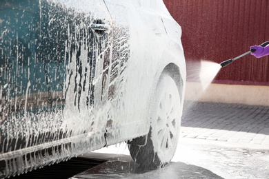 Photo of Worker cleaning automobile with high pressure water jet at car wash