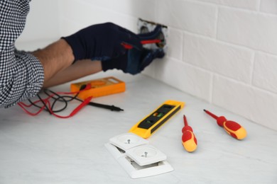 Photo of Electrician with screwdriver repairing power socket indoors, focus on plugs