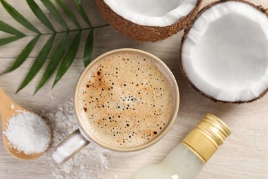 Photo of Cup of coffee, halves of coconut, flakes, bottle of syrup and green leaves on white wooden table, flat lay