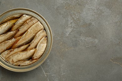 Photo of Sprats in tin can on grey textured table, top view. Space for text