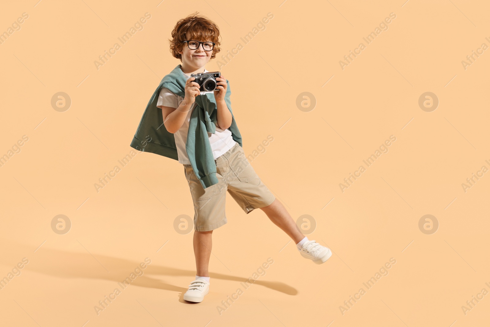 Photo of Fashion concept. Stylish boy with vintage camera on pale orange background. Space for text