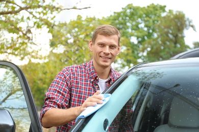Man washing car windshield with rag outdoors