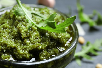 Photo of Bowl of tasty arugula pesto on table, closeup