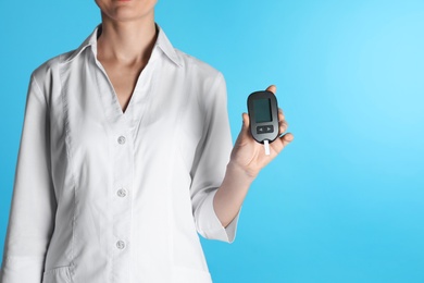 Photo of Female doctor holding digital glucometer on color background, closeup view with space for text. Medical object