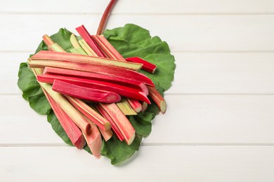 Many cut rhubarb stalks and leaf on white wooden table, above view. Space for text