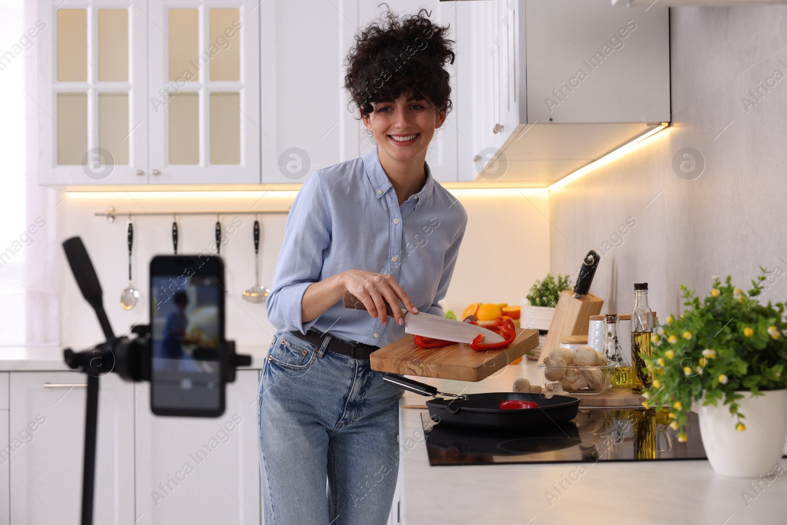 Photo of Smiling food blogger cooking while recording video in kitchen