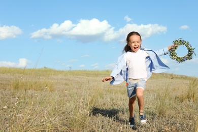 Photo of Cute little girl with flower wreath outdoors, space for text. Child spending time in nature