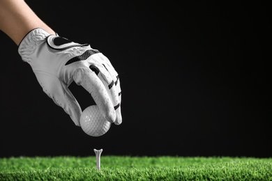 Player putting golf ball on tee against black background, closeup. Space for text
