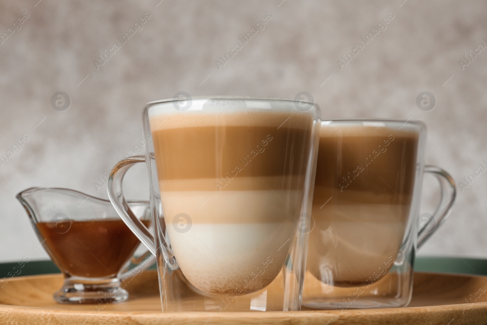 Photo of Tray with glass cups of caramel macchiato and syrup in gravy boat on table