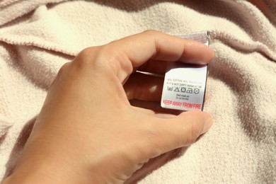 Photo of Woman holding clothing label on beige garment, closeup