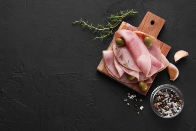 Photo of Tasty ham with olives, garlic, thyme and spices on black textured table, flat lay. Space for text