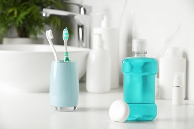 Photo of Mouthwash, toothbrushes and dental floss on white countertop in bathroom
