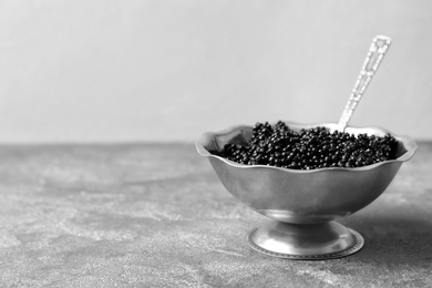 Metal bowl with black caviar on grey background