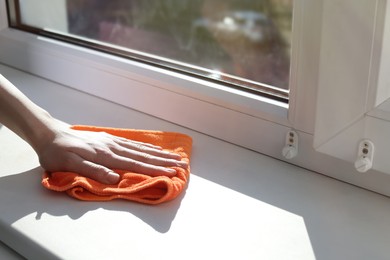 Woman cleaning window sill with rag at home, closeup. Space for text