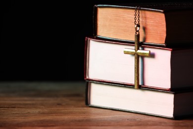 Cross and stack of books on wooden table against black background, closeup with space for text. Religion of Christianity