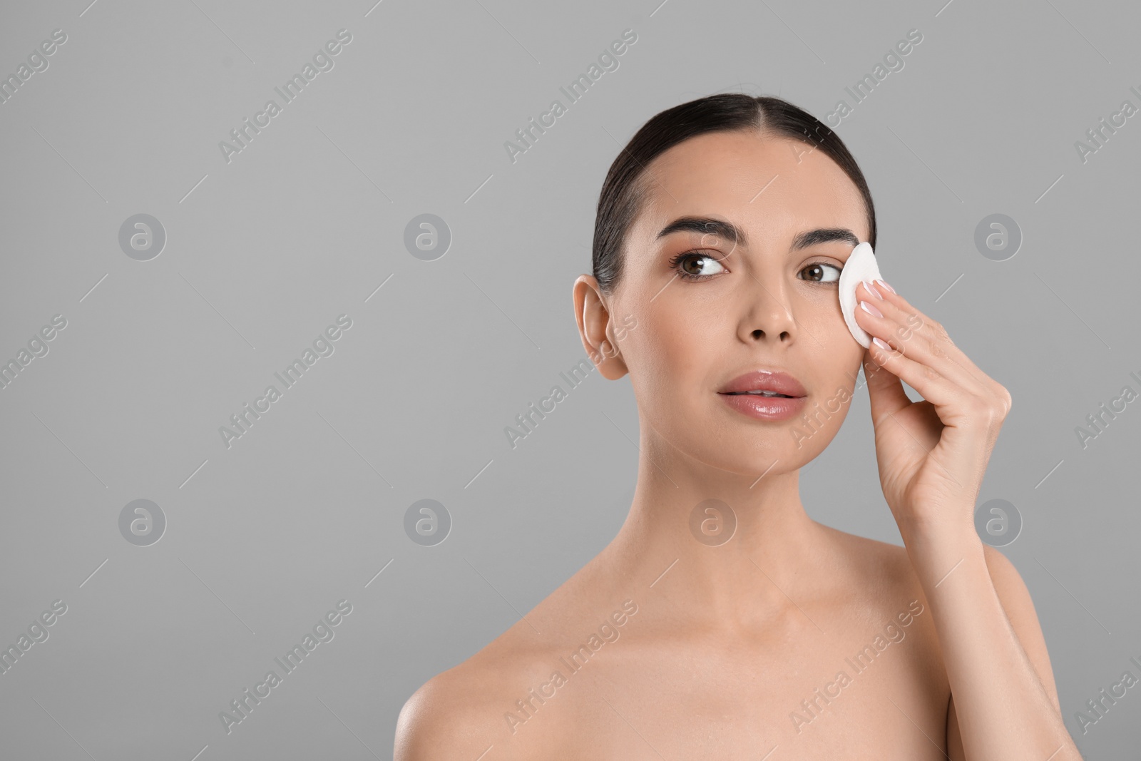 Photo of Beautiful woman removing makeup with cotton pad on light grey background, space for text