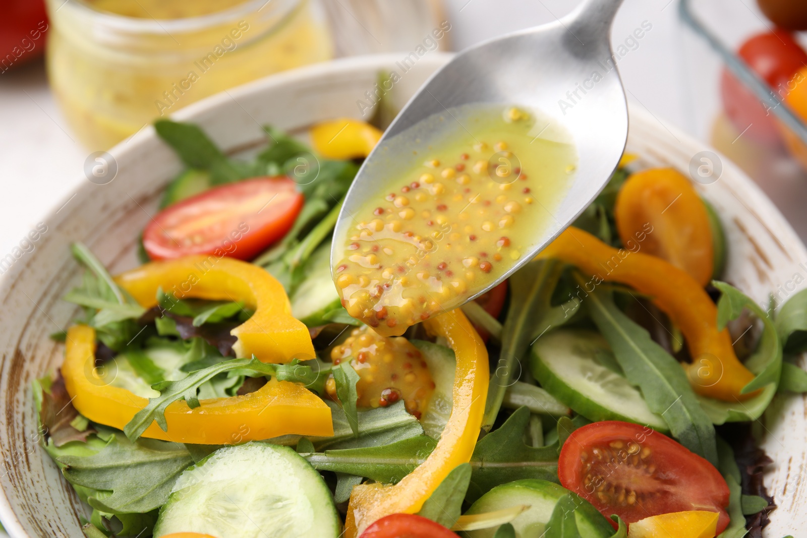 Photo of Pouring tasty vinegar based sauce (Vinaigrette) from spoon into bowl with salad at table, closeup