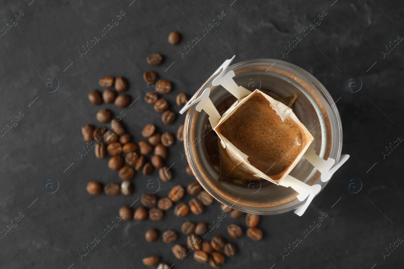 Photo of Glass cup with drip coffee bag on black table, top view