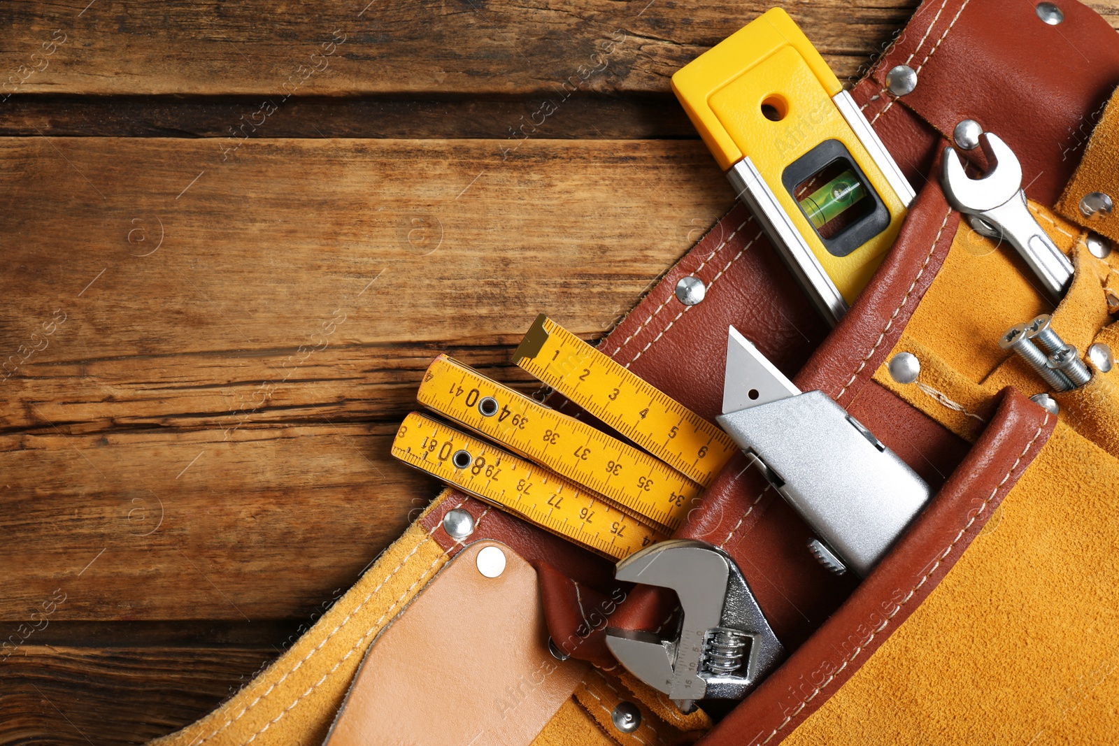 Photo of Belt with utility knife and different tools on wooden table, top view. Space for text