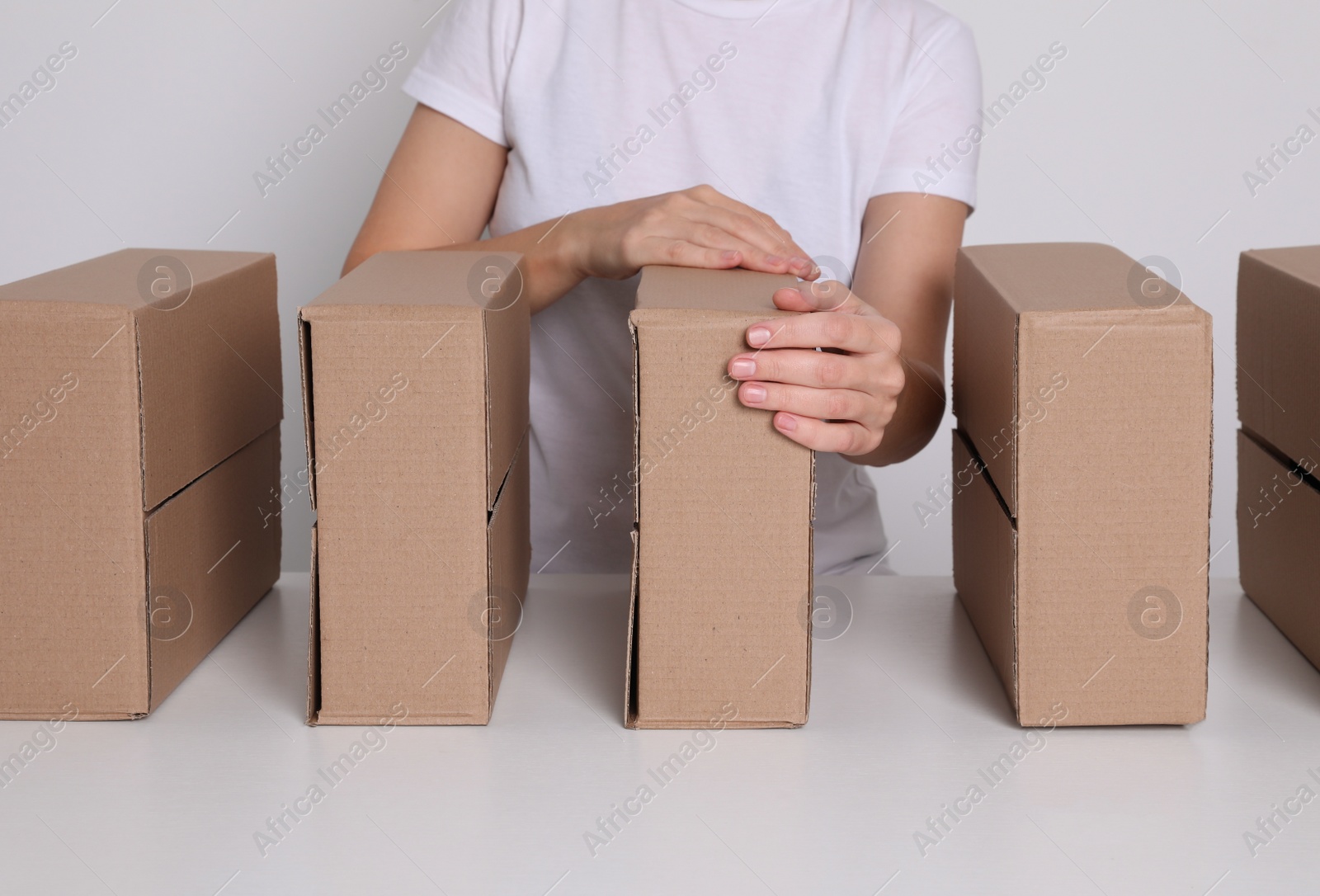Photo of Woman folding cardboard boxes at white table, closeup. Production line