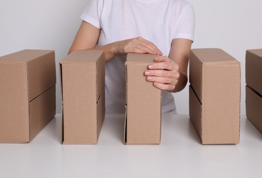 Woman folding cardboard boxes at white table, closeup. Production line