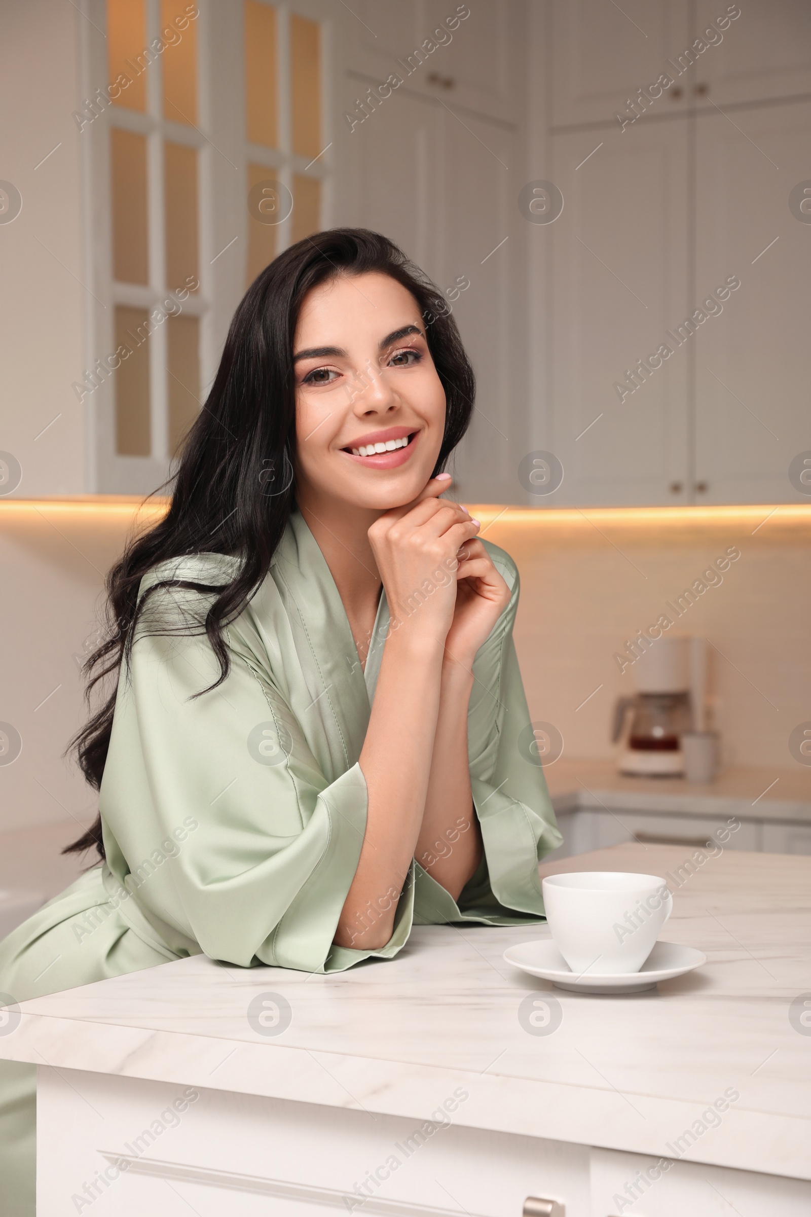 Photo of Pretty young woman wearing beautiful silk robe with cup of coffee in kitchen