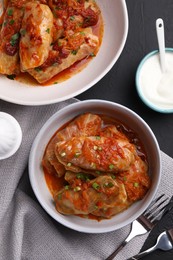 Photo of Delicious stuffed cabbage rolls cooked with homemade tomato sauce on black table, flat lay