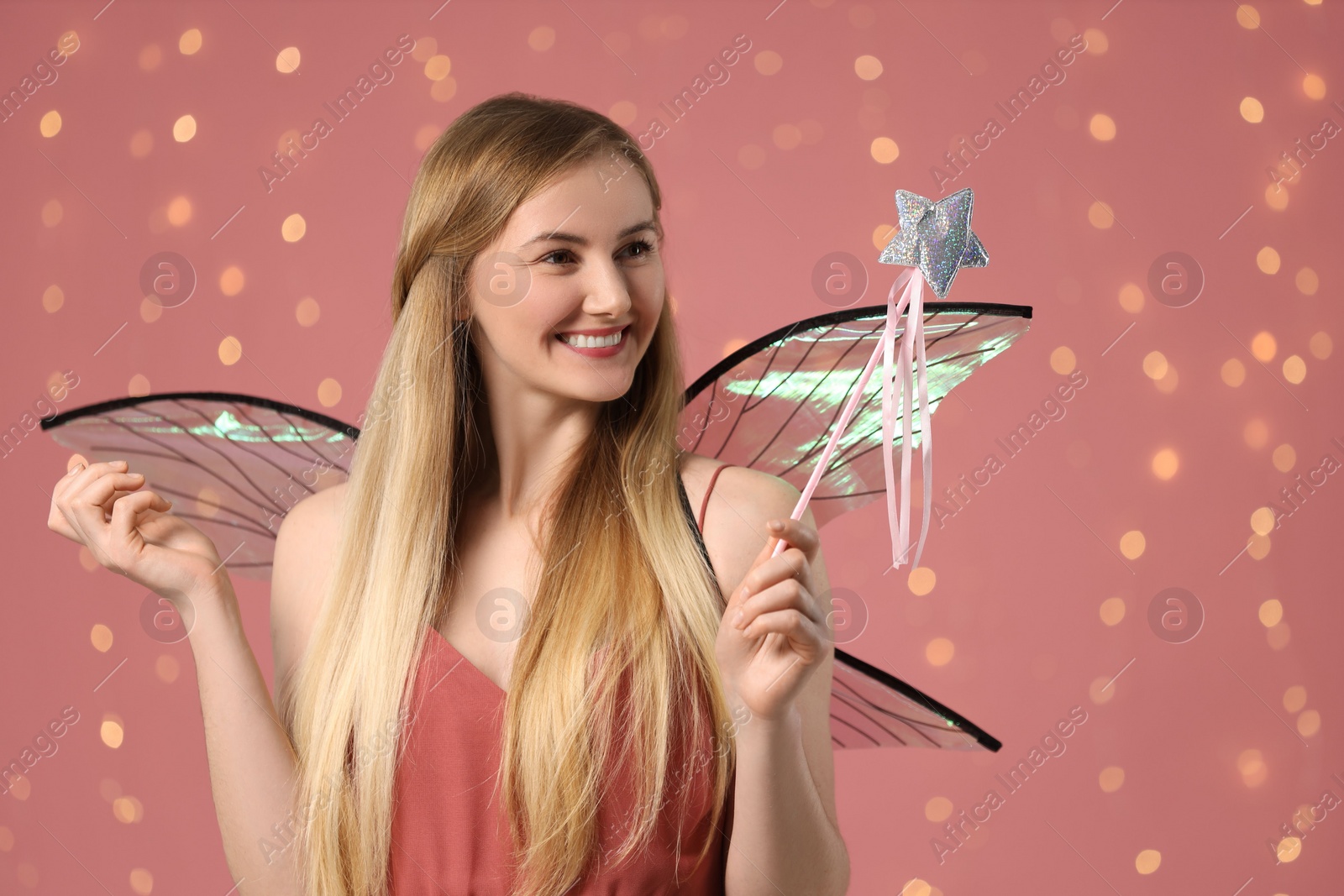 Photo of Beautiful girl in fairy costume with wings and magic wand on pink background