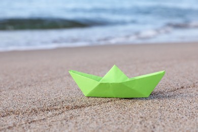 Photo of Light green paper boat near sea on sandy beach