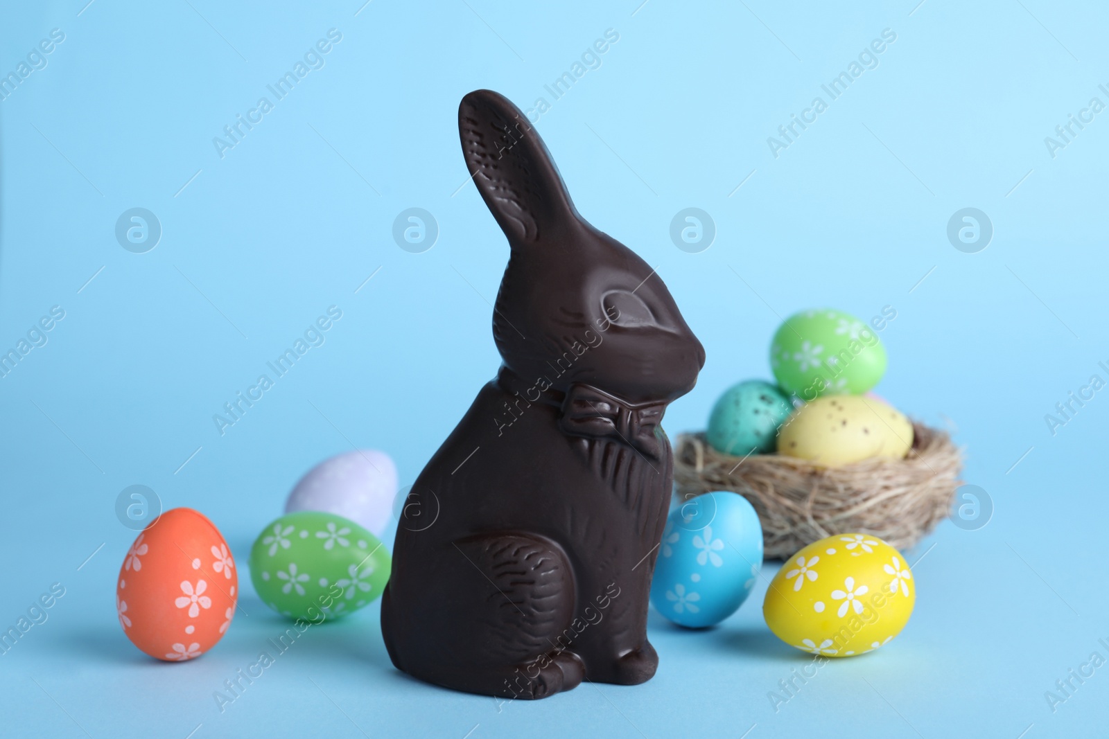 Photo of Dark chocolate Easter bunny and dyed eggs on light blue background