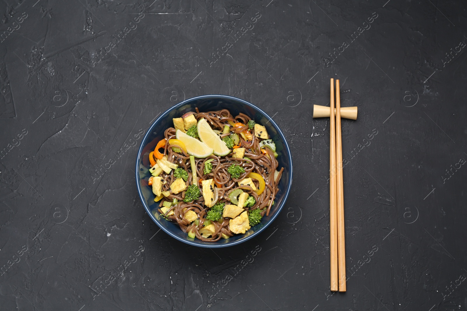 Photo of Stir-fry. Delicious cooked noodles with chicken and vegetables in bowl served on gray textured table, flat lay