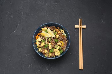 Photo of Stir-fry. Delicious cooked noodles with chicken and vegetables in bowl served on gray textured table, flat lay