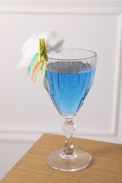 Photo of Bright cocktail in glass decorated with cotton candy and sour rainbow belt on wooden table, closeup