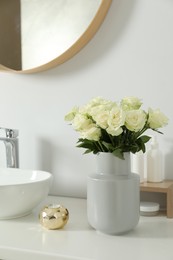 Photo of Vase with beautiful white roses and toiletries near sink in bathroom