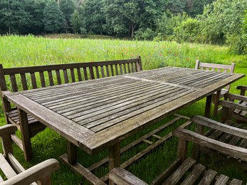 Photo of Wooden table with bench and chairs in garden. Landscape design